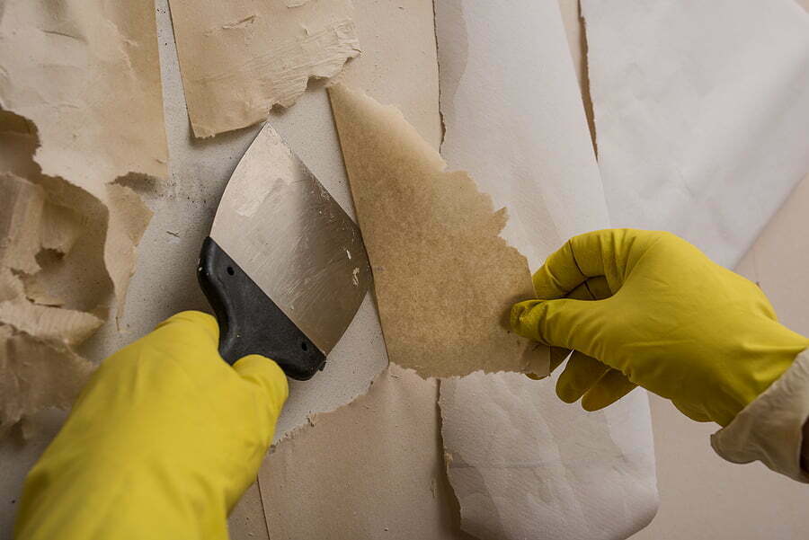 Preparing the wall for painting or sticking new wallpaper. Man in yellow gloves with a scraper in the process of removing old wallpaper. wetted with a special solution surface